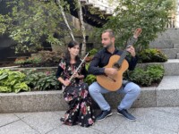 Performances a woman with a flower dress holding a flute and a man looking at her holding and a guitar
